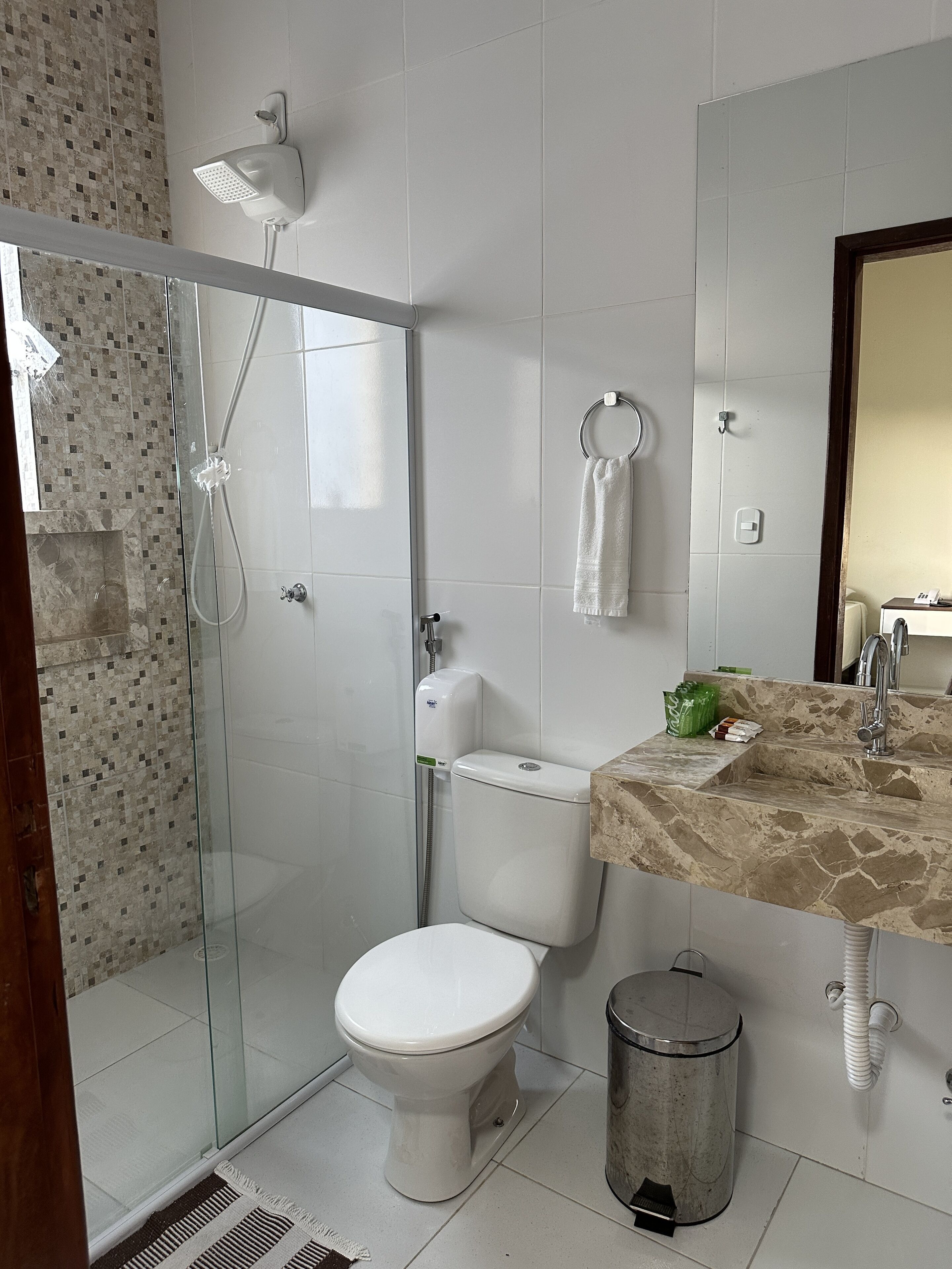 Ein Badezimmer mit einer Duschkabine, Toilette, Waschbecken mit Marmorplatte und einem Mülleimer.