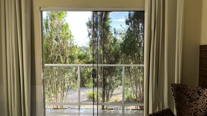 Una habitación con un amplio ventanal corredera que da a un balcón, un sillón estampado y suelo de baldosas.