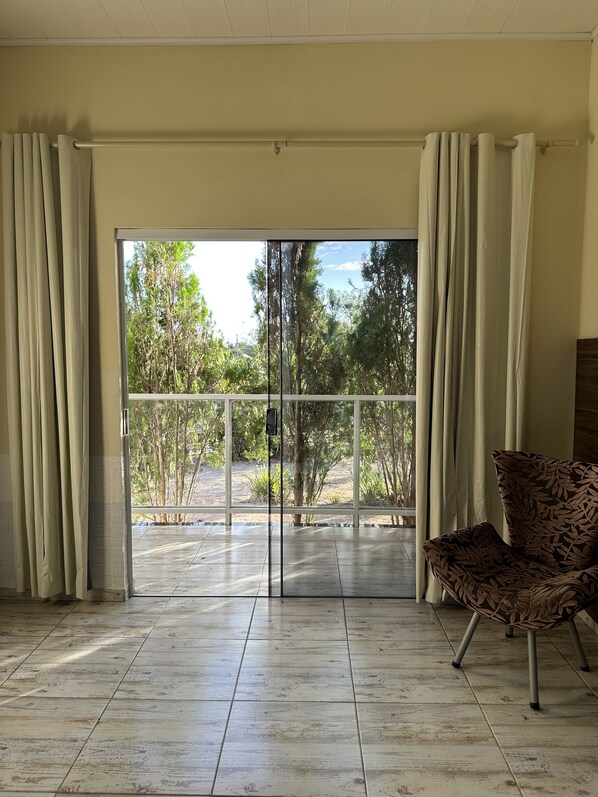 A room with a large sliding glass door leading to a balcony, a patterned chair, and a tiled floor. - Hotel São Francisco (Piranhas)