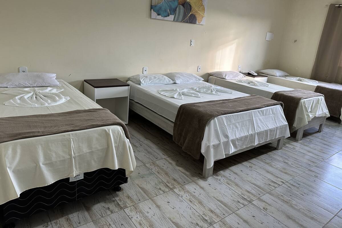 Ett hotellrum med fyra sängar, var och en med ett vitt överkast och en brun filt. Det hänger en tavla på väggen ovanför sängarna.