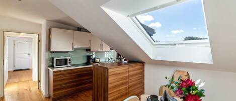 A modern kitchen with a skylight, wooden cabinets, and a dining area with a table and chairs.