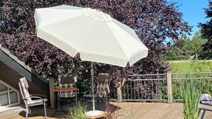 Een houten terras met buitenmeubilair, een witte parasol en plantenpotten.