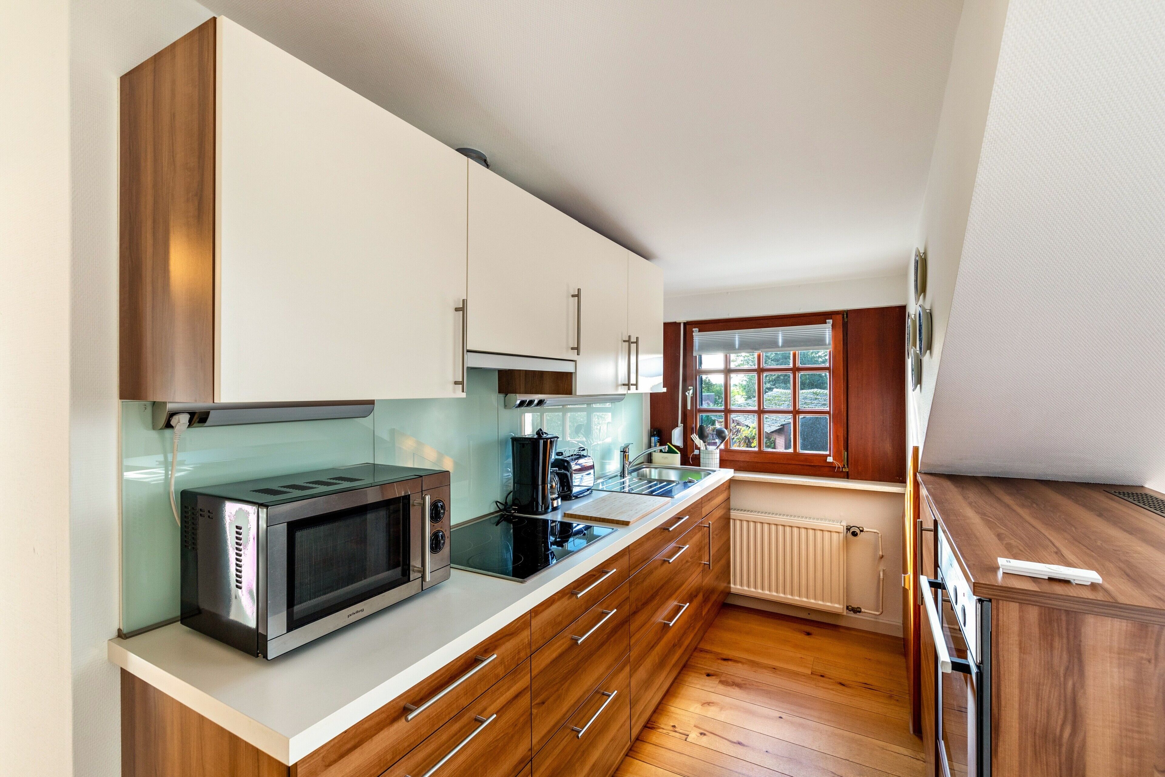 Een moderne keuken met houten kastjes, een magnetron, een koffiezetapparaat en een raam met zonwering.