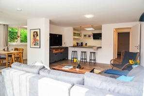 A modern living room with a sofa, a dining table, and a kitchen area with bar stools.