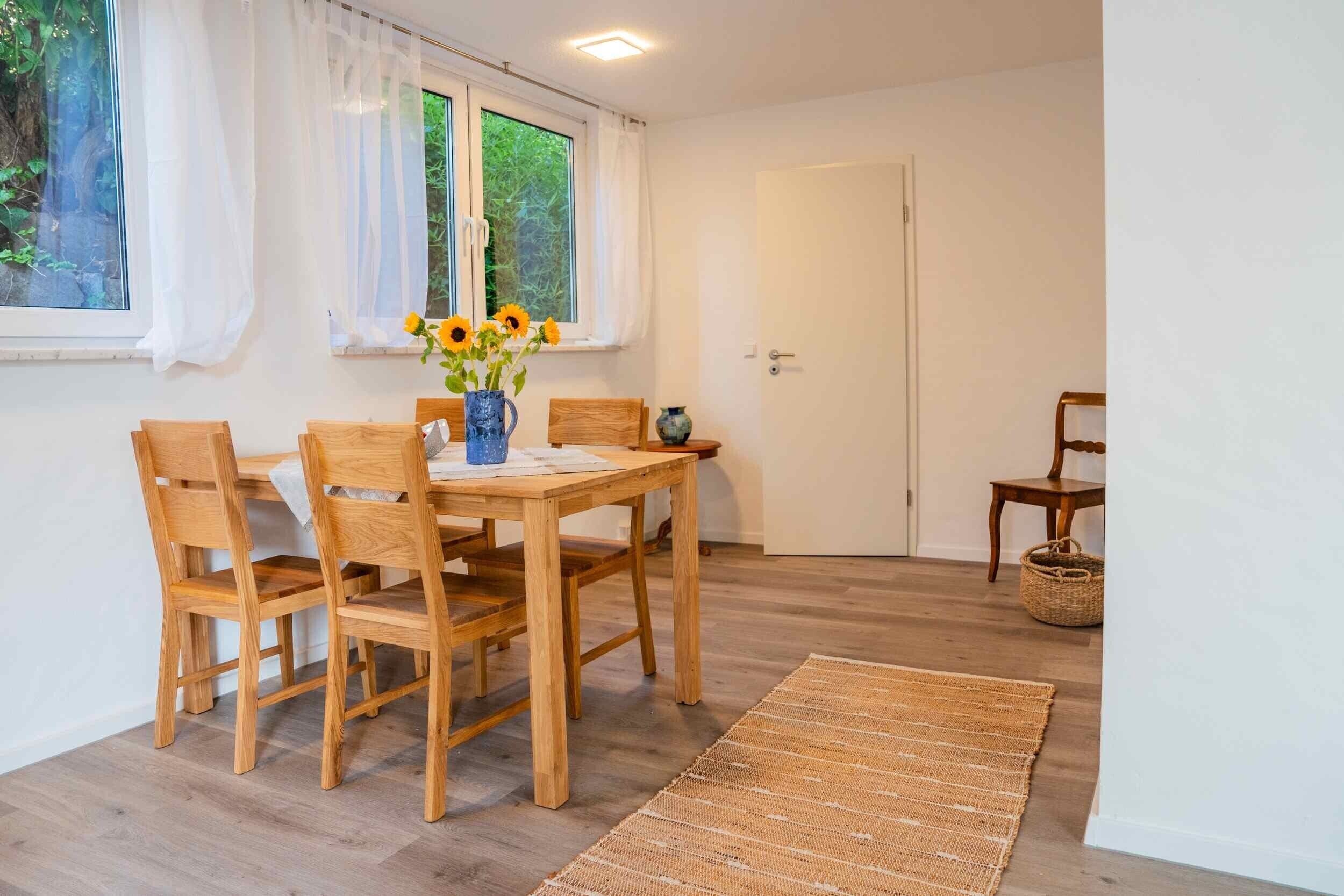 Ein Essbereich mit einem Holztisch und Stühlen, einer Vase mit Blumen und einem Fenster mit Vorhängen.