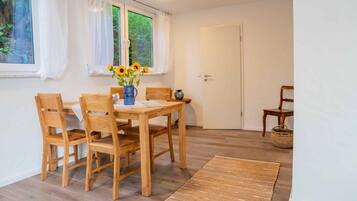 Ein Essbereich mit einem Holztisch und Stühlen, einer Vase mit Blumen und einem Fenster mit Vorhängen.