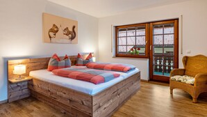 A bedroom with a wooden bed, a nightstand with a lamp, a wicker chair, and a window with a view.