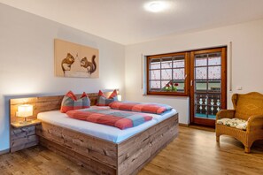 A bedroom with a wooden bed, a nightstand with a lamp, a wicker chair, and a window with a view.