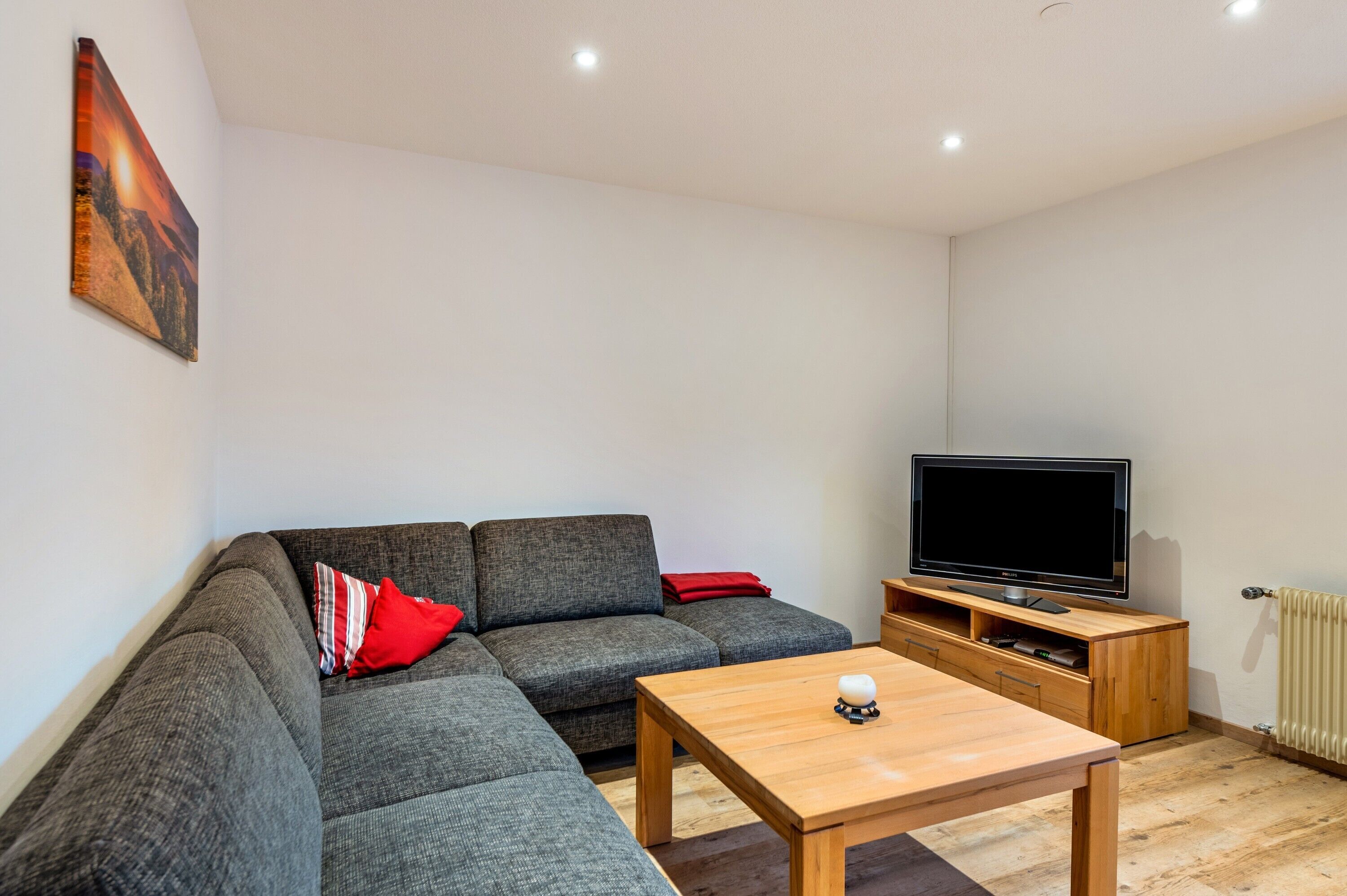 Ein modernes Wohnzimmer mit einem Ecksofa, einem Flachbildfernseher, einem Holztisch und einem Gemälde an der Wand.
