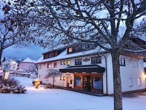 A snow-covered building with a traditional architectural style, a visible entrance, and a well-lit facade.