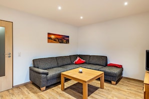 A modern living room with a grey sofa, a wooden coffee table, and a painting on the wall.