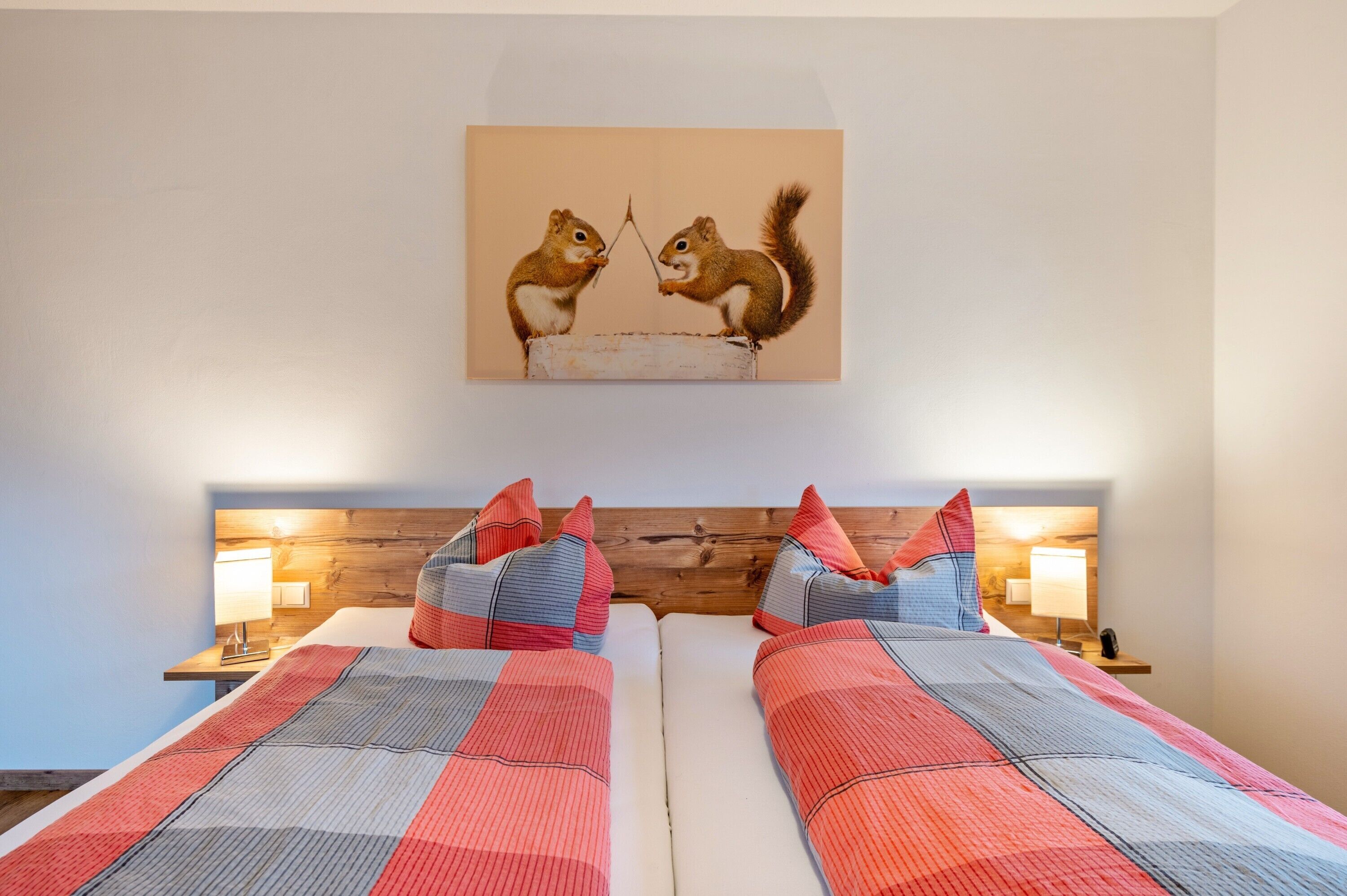 Une chambre d’hôtel avec deux lits, une tête de lit en bois et un tableau représentant des écureuils accroché au mur.