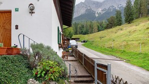 Ein Gebäude mit einer Holztür, einer Treppe, die zu einer Veranda führt, und Blick auf einen Berg.
