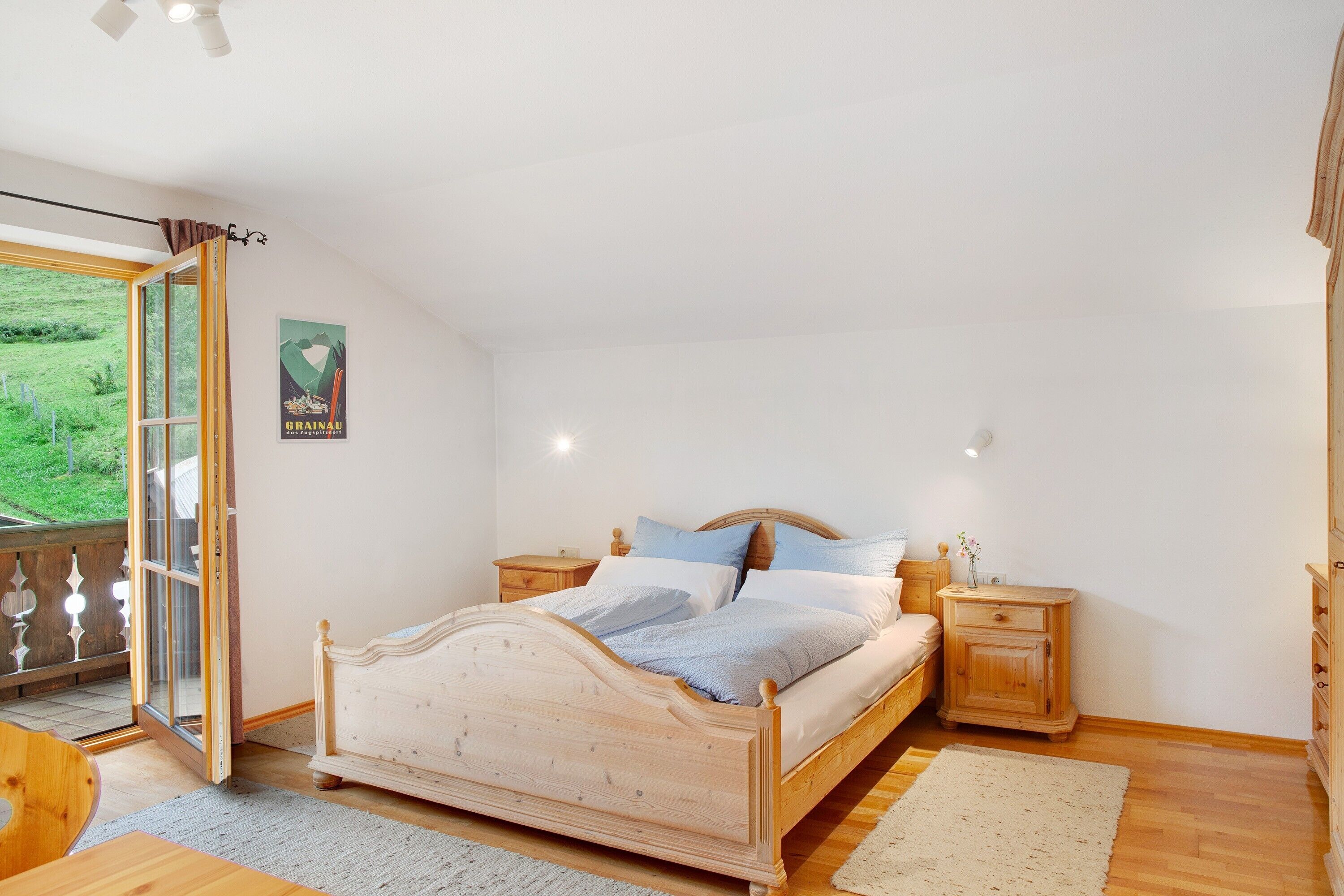 Een slaapkamer met een houten bed, twee nachtkastjes, een grote raam met uitzicht op groen en een poster aan de muur.