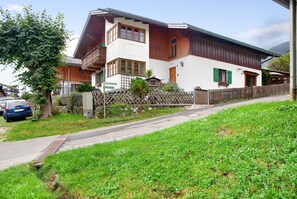 Een houten huis met twee verdiepingen, een balkon, een stenen hek en een verharde oprit.