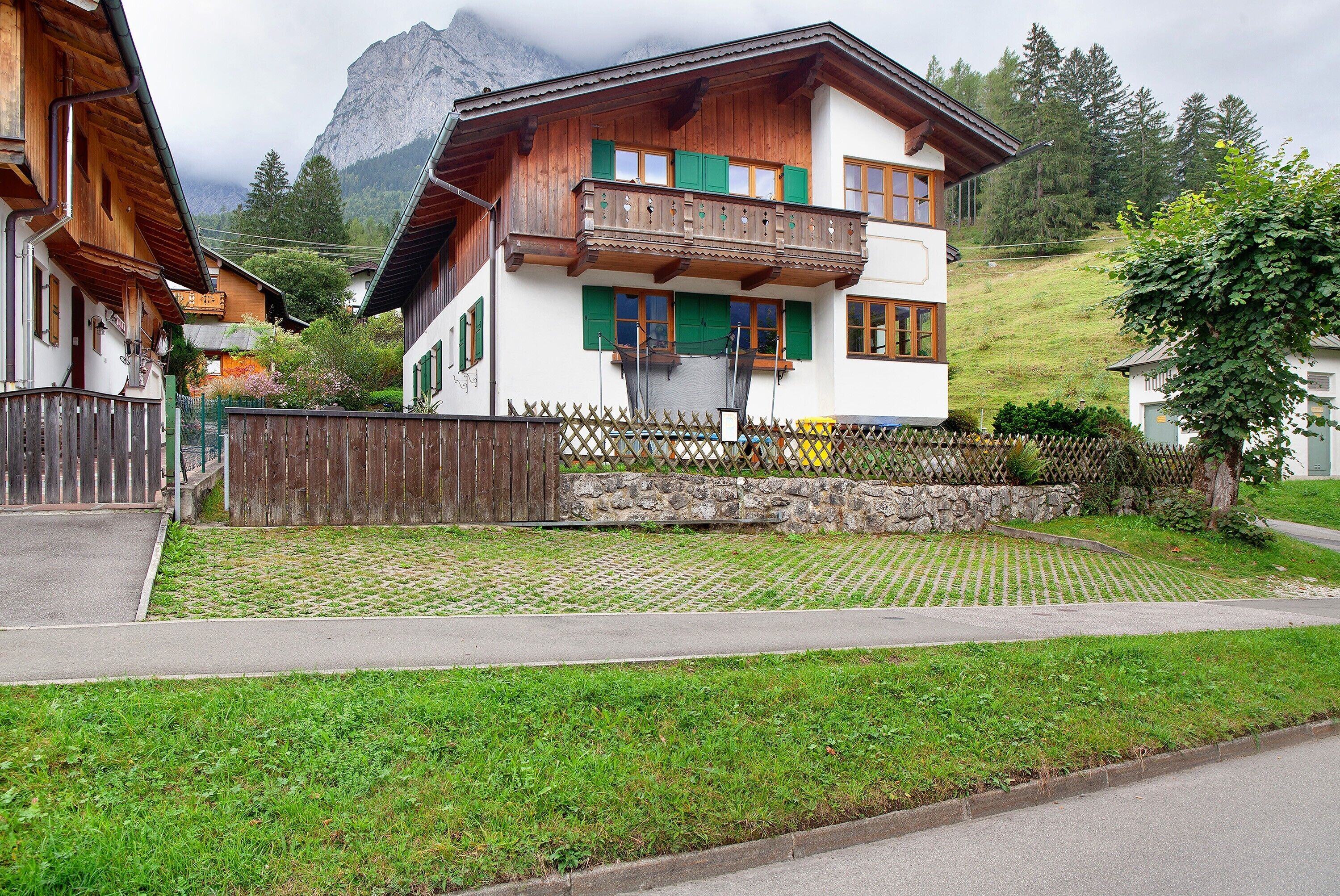 Ein zweistöckiges Gebäude mit Balkon, Steinmauer und einer Rasenfläche davor.