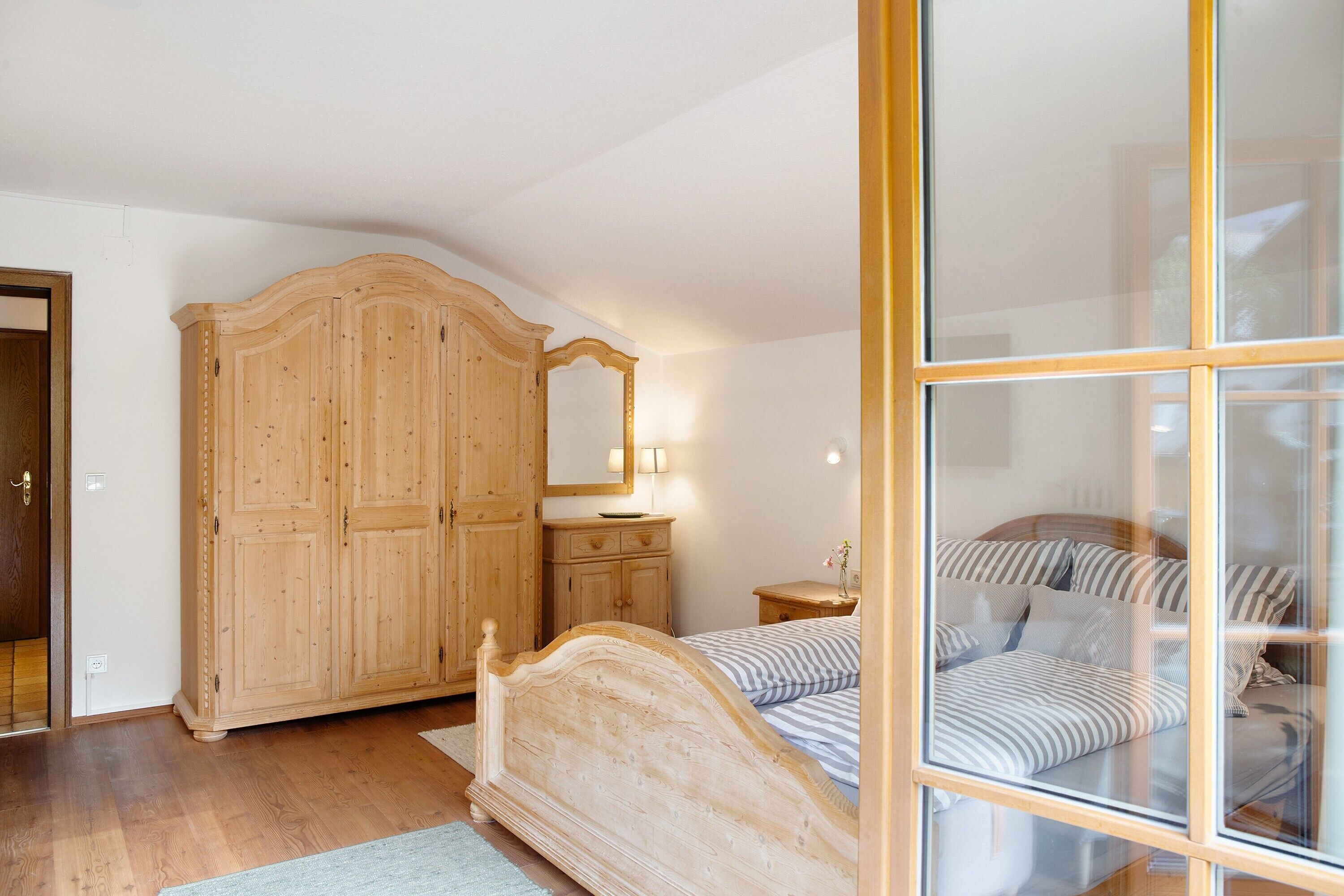 Ein Schlafzimmer mit Holzschrank, Nachttisch, Lampe und einem Bett mit gestreifter Bettwäsche.