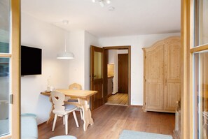 Una habitación con una mesa de comedor de madera, sillas, un televisor instalado en la pared y un armario.