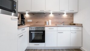 A modern kitchen with white cabinetry, a built-in oven, a microwave, and a coffee maker. - Holiday Apartment "Finsterwalde" (FInsterwalde)