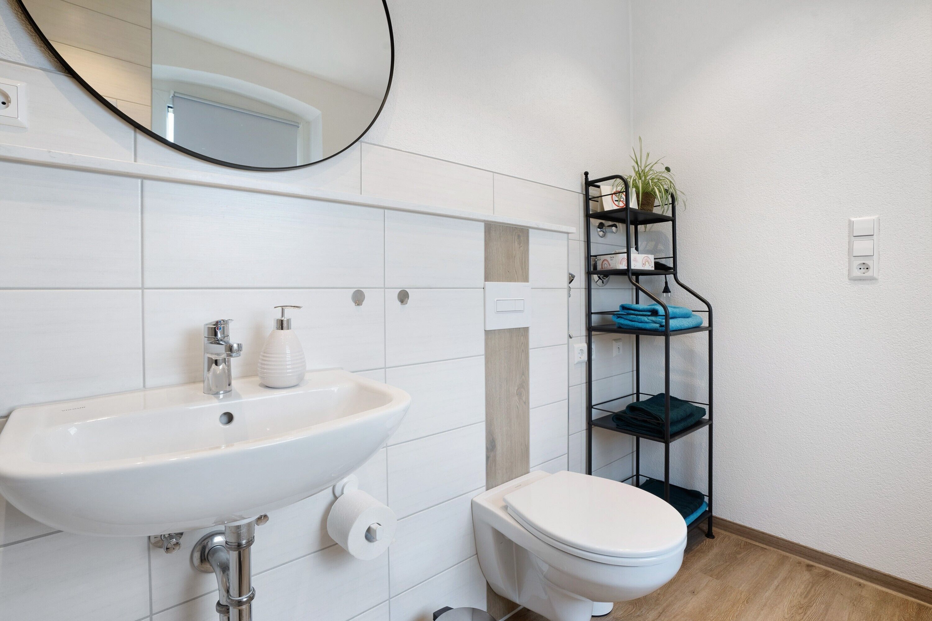 A bathroom with a white sink, toilet, and a shelf with folded towels.
