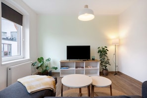Ett vardagsrum med en tv, två runda bord, en soffa, ett element, ett fönster och en golvlampa.