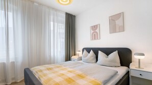 A bedroom with a bed, bedside tables, a lamp, a window with curtains, and wall art. - Holiday Apartment "Finsterwalde" (FInsterwalde)