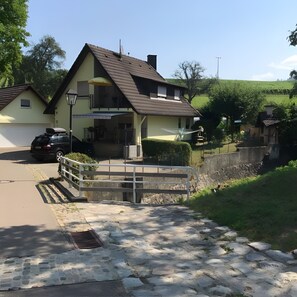 Une maison à deux étages avec un toit en pente, un garage et une allée pavée menant à un pont en pierre.