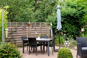 Une terrasse extérieure avec une table et des chaises, entourée d’une clôture en bois et d’une végétation luxuriante.