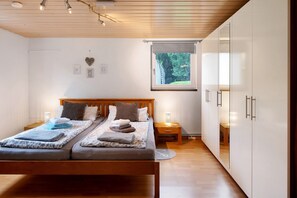 Une chambre à coucher avec un lit en bois, deux tables de chevet, une fenêtre donnant sur un beau paysage et une armoire.
