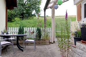 Une terrasse extérieure avec une table et des chaises, une clôture blanche en bois et diverses plantes en pot.