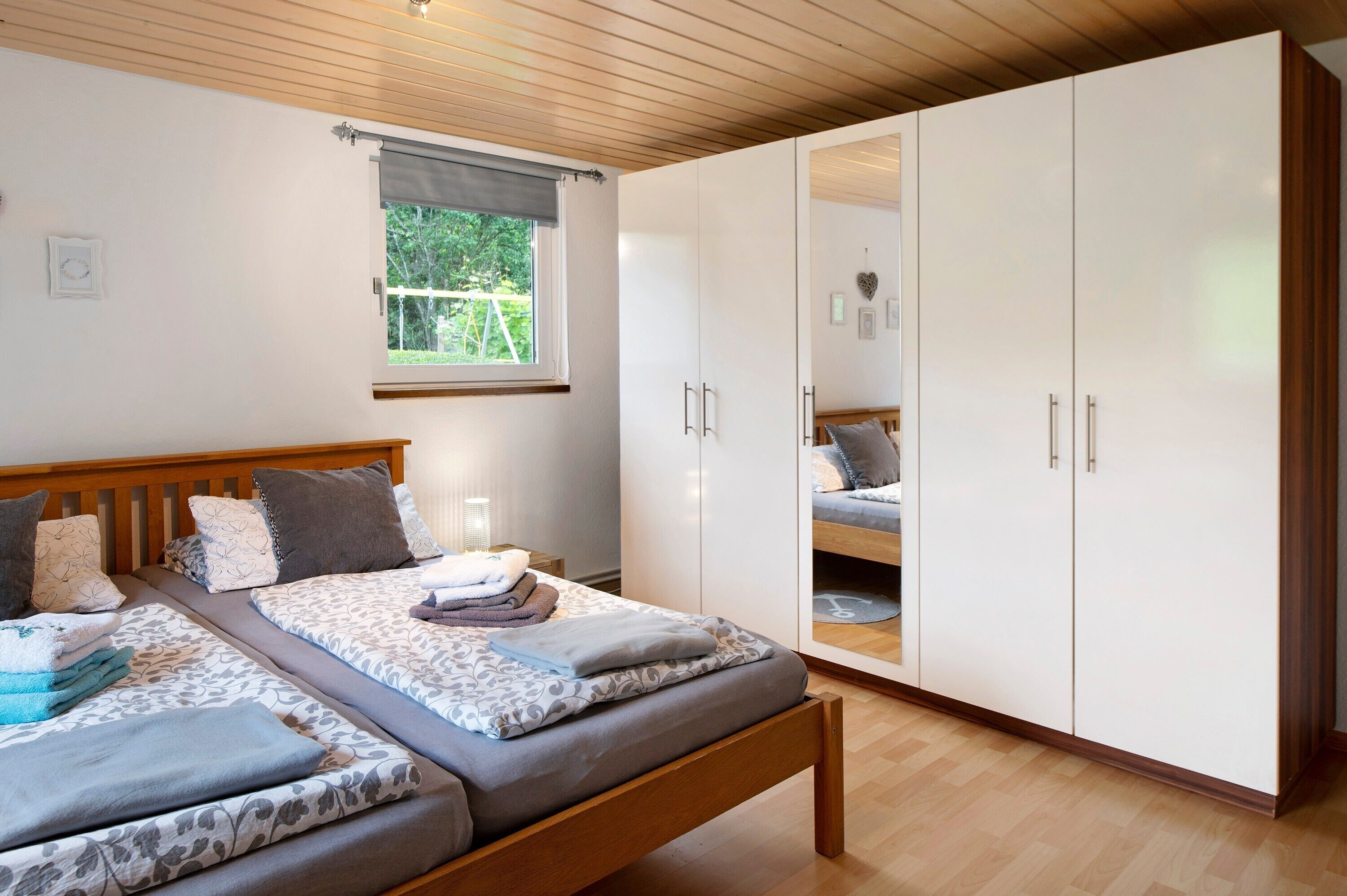 A bedroom with two beds, a window, wooden ceiling, and white wardrobes.