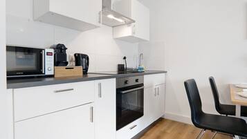 Una cocina moderna con armarios blancos, microondas, cafetera y comedor con sillas negras.