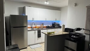 A compact kitchen with white cabinets, a stainless steel refrigerator, a microwave, and a small island with a sink.