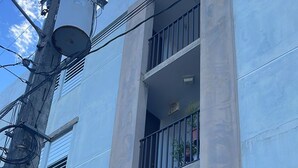 A multi-story building with a central concrete column, balconies with metal railings, and a visible entrance door.