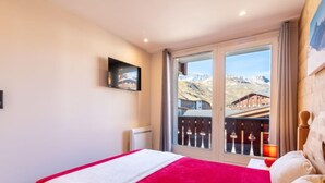 Un dormitorio con cama, televisor montado en la pared y balcón con vistas a montañas.