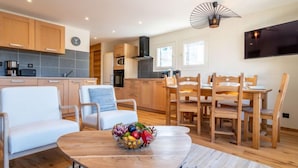 Una cocina moderna con armarios de madera, un comedor con mesa y sillas de madera, y un televisor montado en la pared.