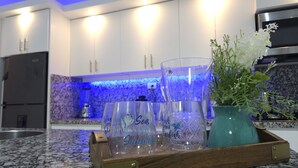 Une cuisine dotée de plans de travail en granit, d’un réfrigérateur en acier inoxydable, de meubles blancs et d’un pare-feu illuminé de lumière bleue.
