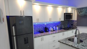 Une cuisine moderne avec des meubles blancs, un réfrigérateur noir, un four à micro-ondes encastré et un plan de travail en granit.