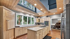 Una cocina amplia con armarios de madera, una isla grande y vistas a zonas verdes a través de las ventanas.