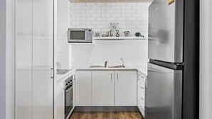 A compact kitchen with white cabinets, a microwave, a sink, and a refrigerator.