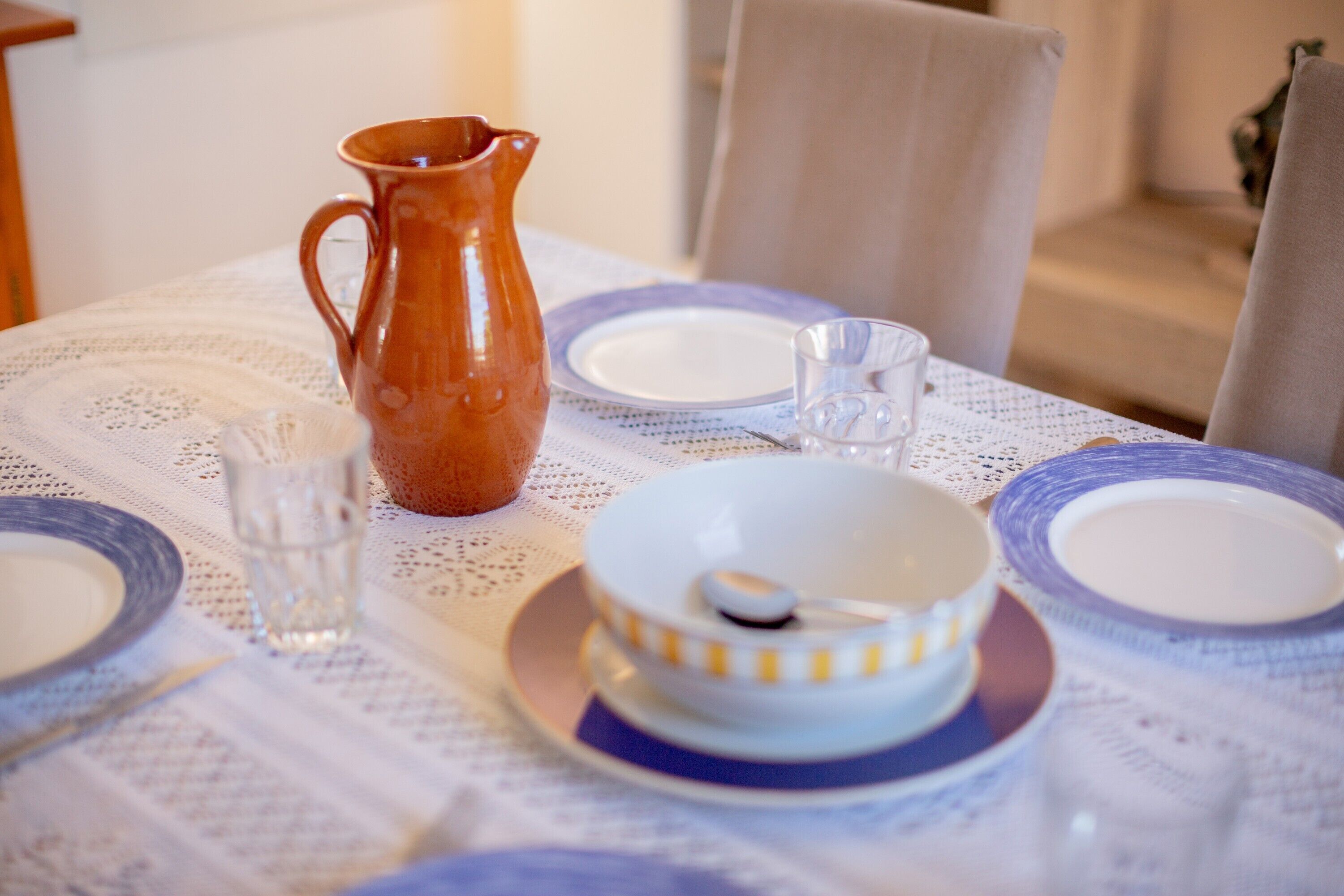Une table dressée avec une carafe, un verre, un bol et des assiettes, le tout posé sur une nappe en dentelle.