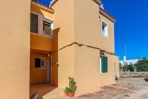 A two-story building with a yellow facade, a small entrance, and a potted plant.