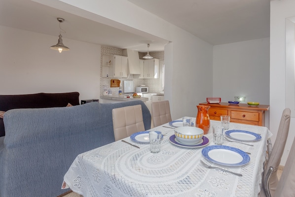 A dining area with a table set for two, a kitchen in the background, and a sofa with a blanket.