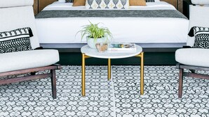 A room with a bed, two armchairs, a round coffee table, and a large wall mural of palm trees. - Mandala Clubhouse (Canggu)