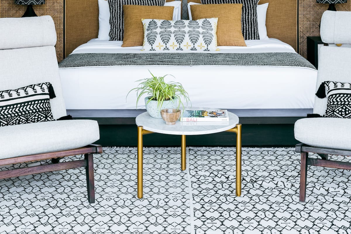 A room with a bed, two armchairs, a round coffee table, and a large wall mural of palm trees.