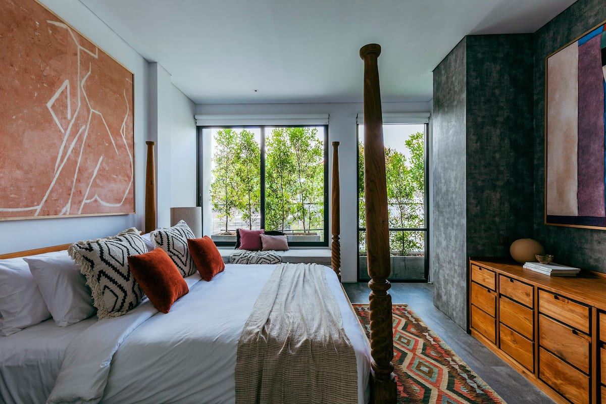 A modern bedroom with a large bed, a wooden wardrobe, and a view of trees through the window.