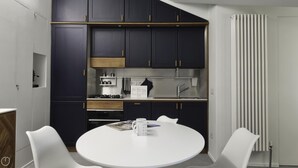 A modern kitchen with dark cabinets, a white countertop, and a round dining table with two chairs. - Italianway Comfort - Torino 48 (Milan)