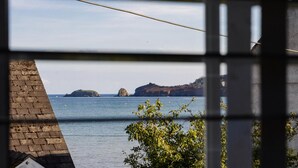 Vista costera a través de una ventana, con un muro de ladrillo y follaje en primer plano.