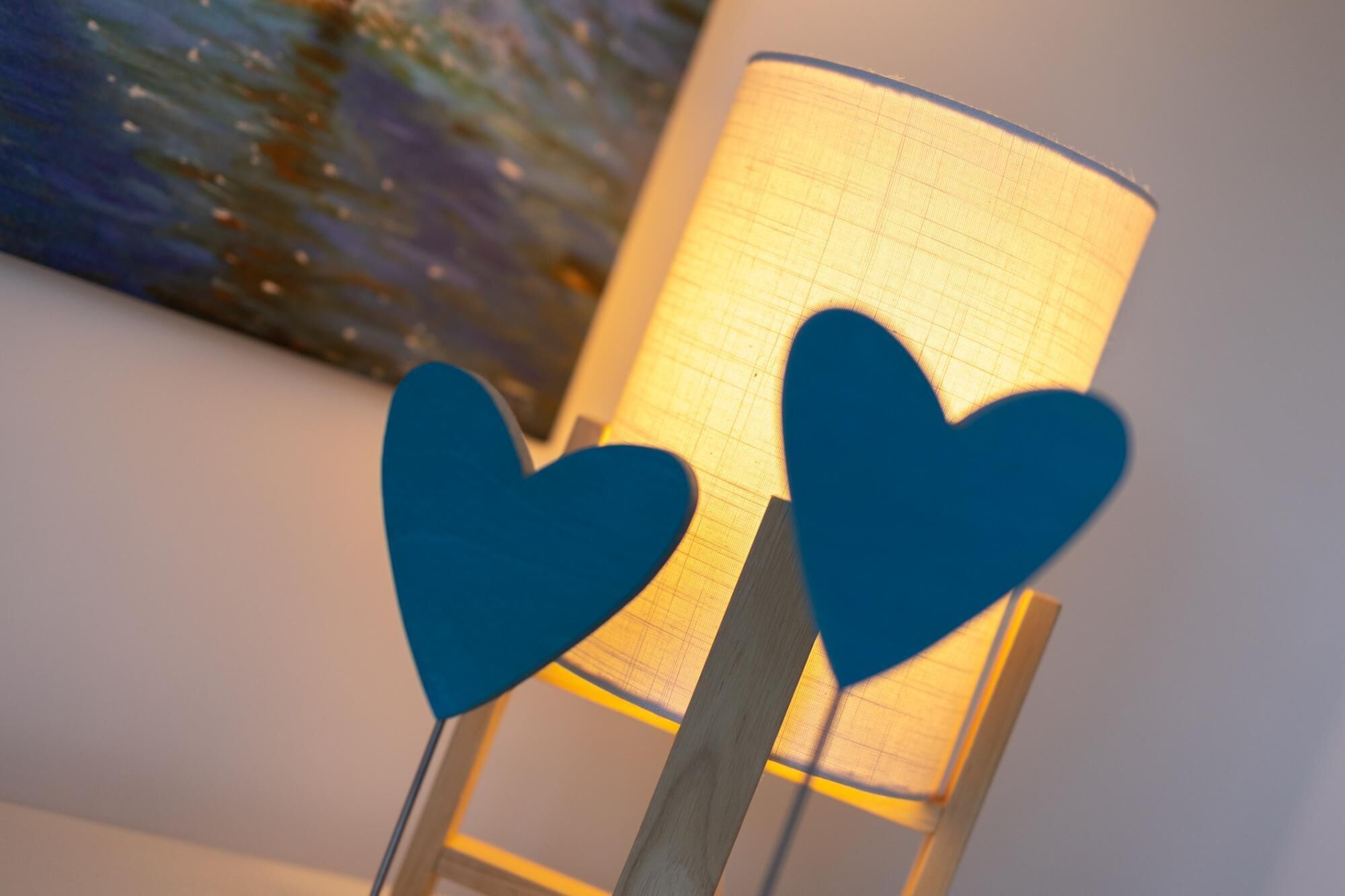 Une lampe dont l’abat-jour présente un motif quadrillé et qui est ornée de deux décorations en forme de cœur sur son pied.