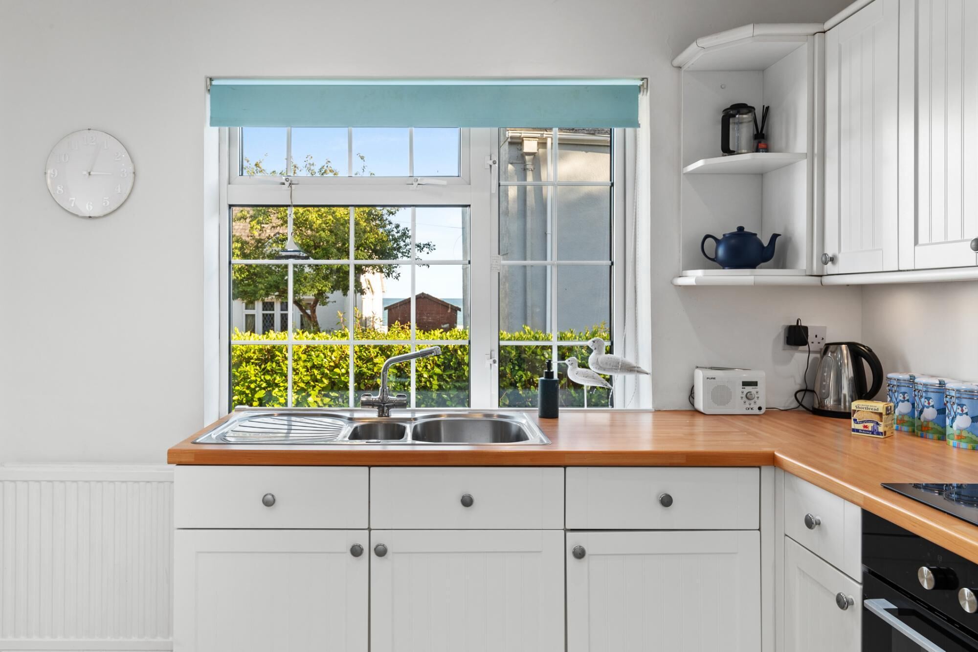 A kitchen with a window, white cabinets, a sink, and a kettle.